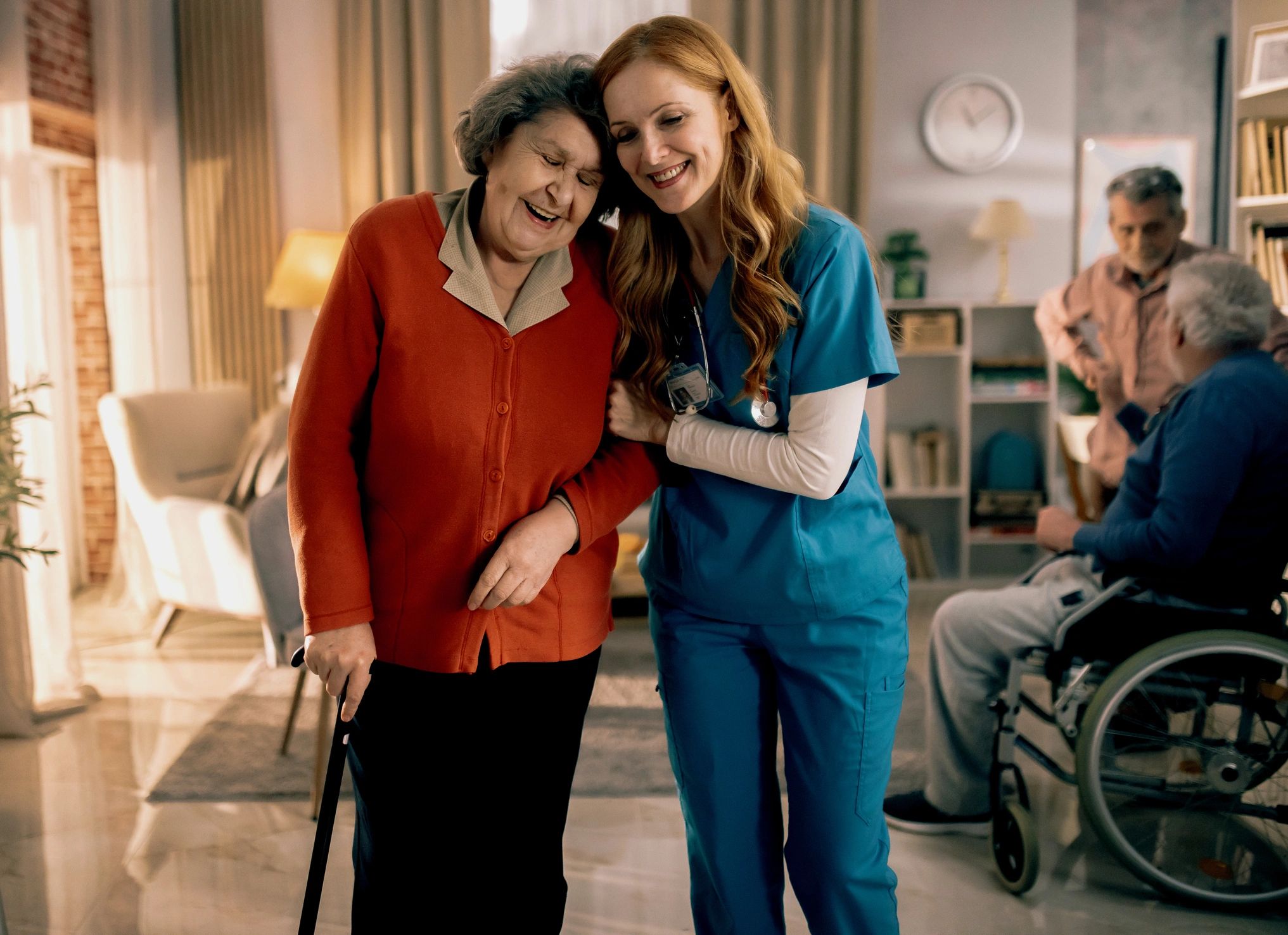 Caregiver assisting a senior woman with walking in a nursing home common room